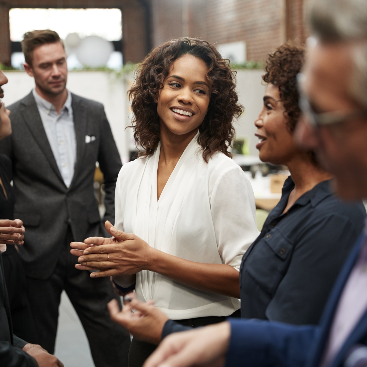 Seven business colleagues in good spirits chatting. In focus are two Black women, a Black man, two white men and a white woman